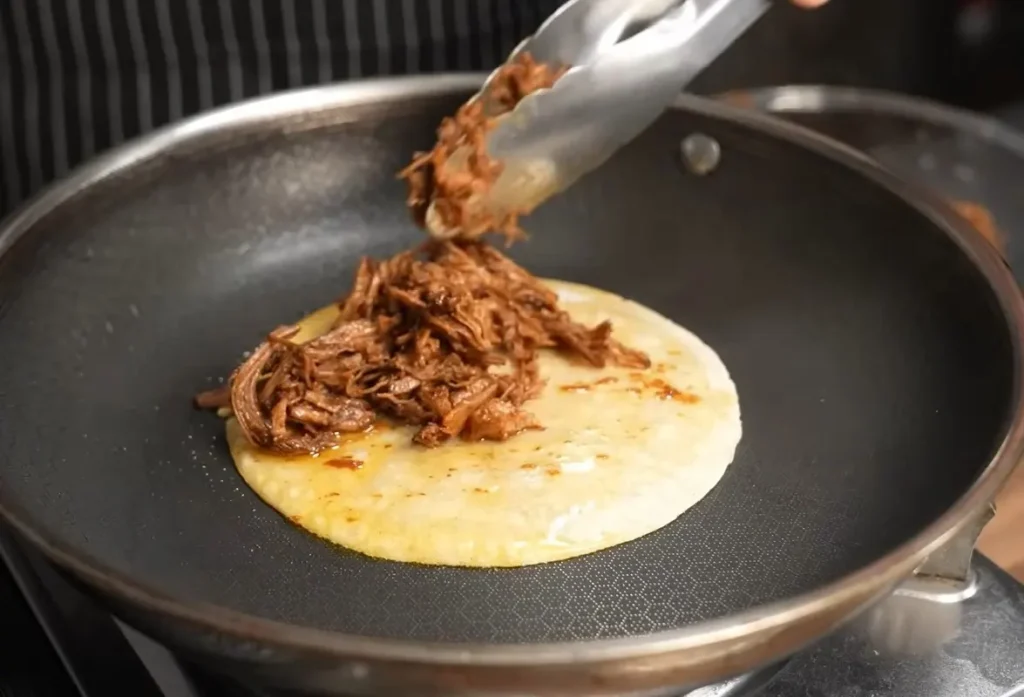 Birria tacos frying in flavorful red birria fat until crispy