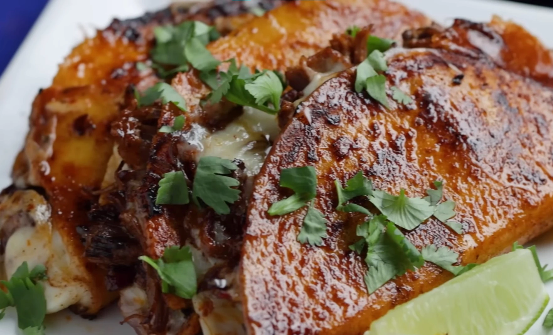 Crispy birria taco frying in a cast iron skillet dipped in red chile fat